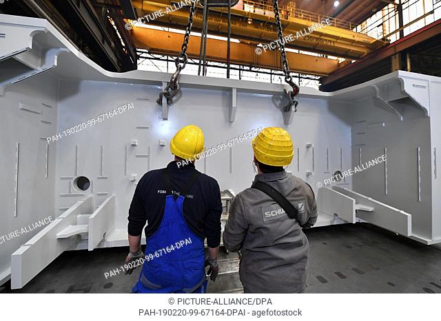 20 February 2019, Thuringia, Erfurt: Two employees transport the component of a large press by crane in a production hall of Schuler Pressen GmbH