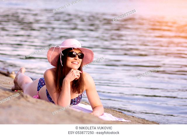 The smiling sunbathing woman is enjoying in the summer lying down on sand on the beach
