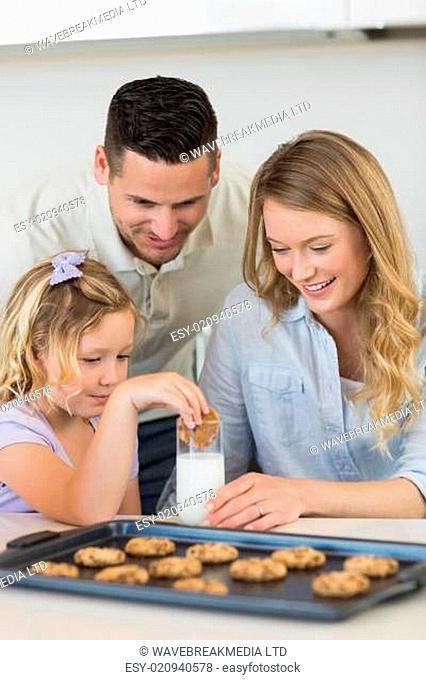 Parents looking at daughter dipping cookie in milk