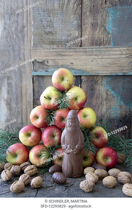 A homemade chocolate Santa Claus in front of a pyramid of apples and pine branches