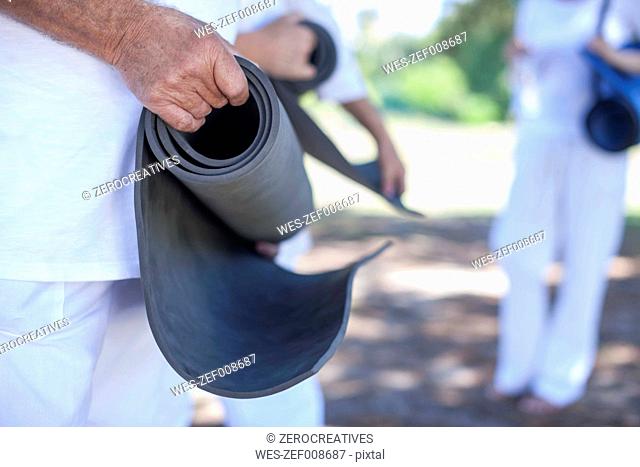 Elderly man rolling up fitness mat outdoors