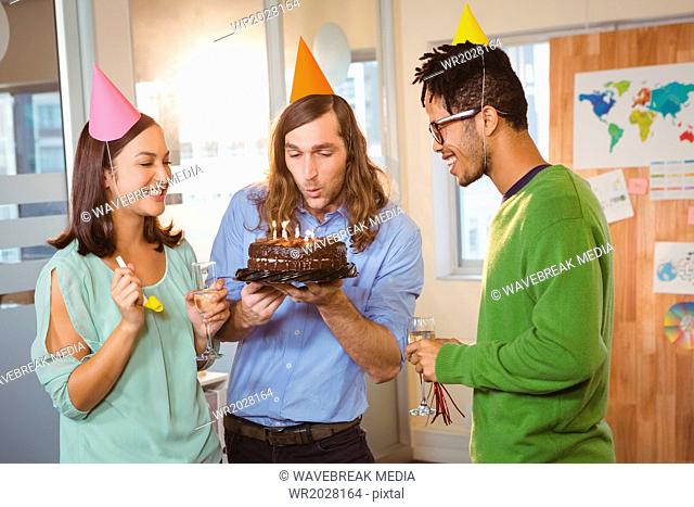 Creative businessman blowing cake in office
