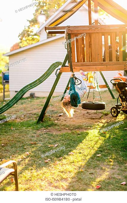 Girl hanging upside down on playground equipment in garden