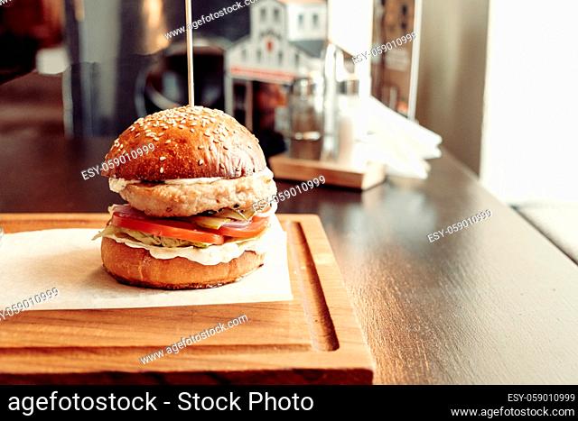 Fresh burger on cutting board as plate over wooden table with copy space