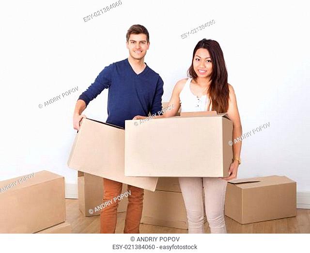 Young Couple Carrying Cardboard Boxes At New Home