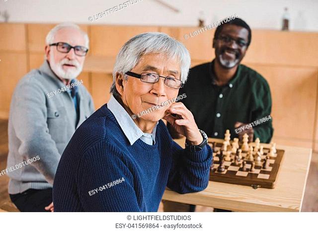 group of happy senior friends playing chess together