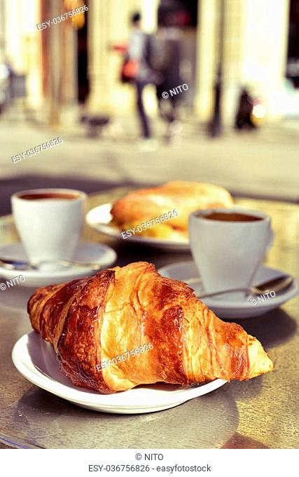 closeup of a table in the terrace of a cafe set for breakfast, with some cups of coffee, a croissant and a spanish omelette sandwich