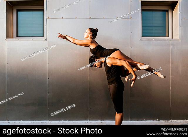 Male gymnast carrying female on shoulders while practicing dance posture by wall