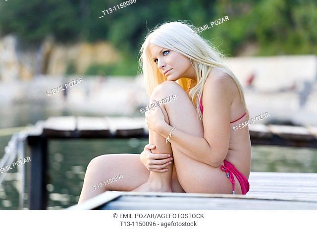 Sitting on a wooden wharf young woman with a long blonde hair