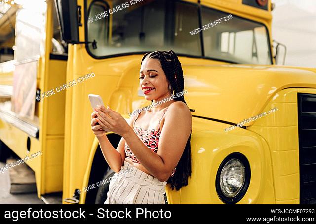 Happy young woman using smart phone leaning on food truck