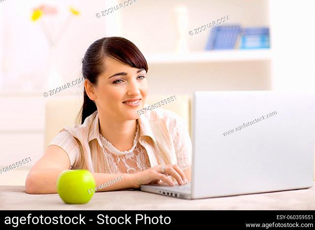 Happy young women browsing internet on laptop computer at home, smiling