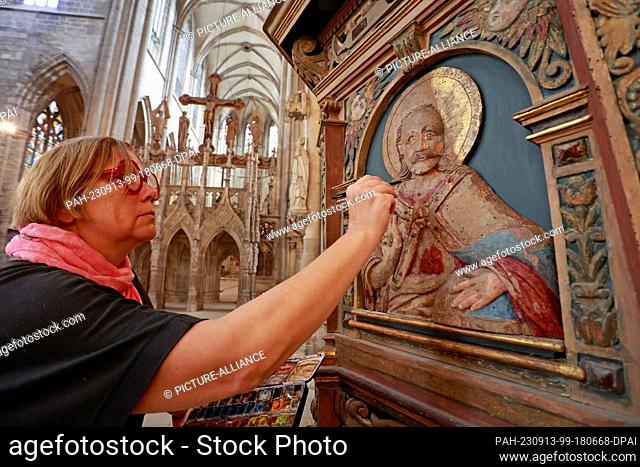 13 September 2023, Saxony-Anhalt, Halberstadt: Restorer Christine Machate is repairing spots on a pulpit relief in Halberstadt Cathedral