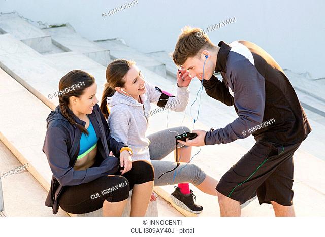 Three friends taking a break from exercising, listening to music on mp3 players