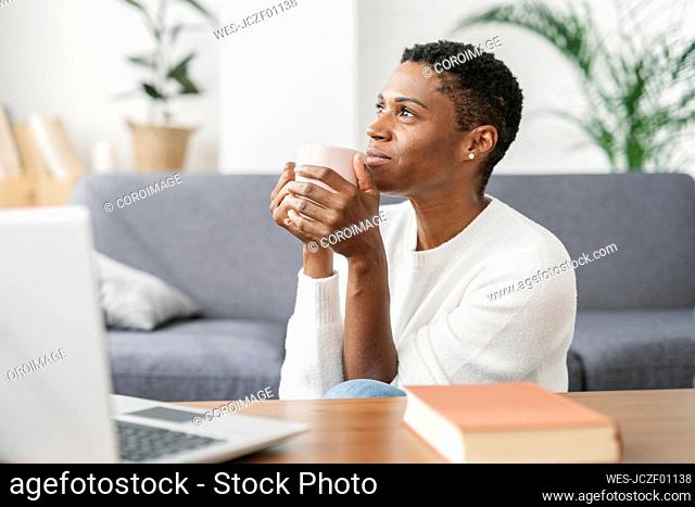 Thoughtful woman holding cup of coffee in loving room at home