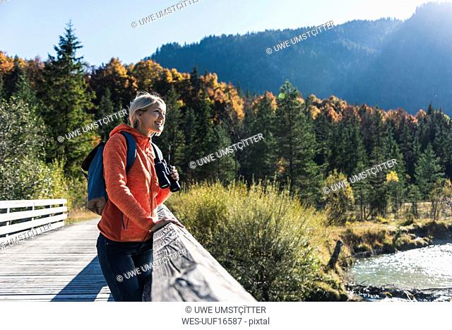 Austria, Alps, woman on a hiking trip standing on a bridge with binoculars
