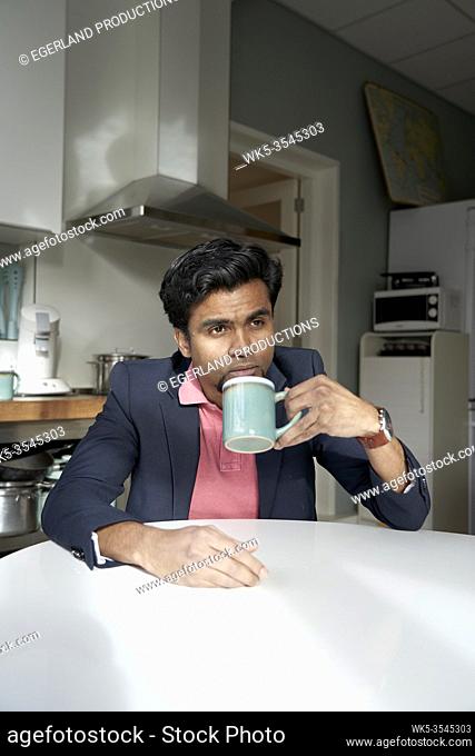 wistful Indian man nipping on cup
