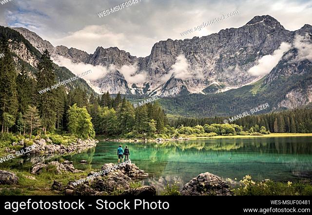 Man and woman standing by lake in mountain landscape