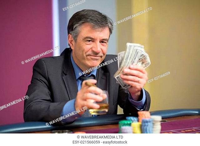 Man holding money smiling at the roulette table in casino