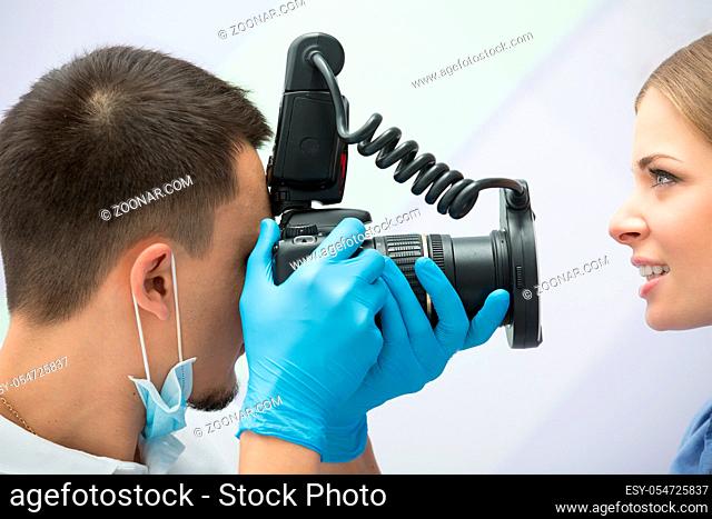 Dentist with camera making shots of patients smile after treatment. Special camera with flash ring shadowless
