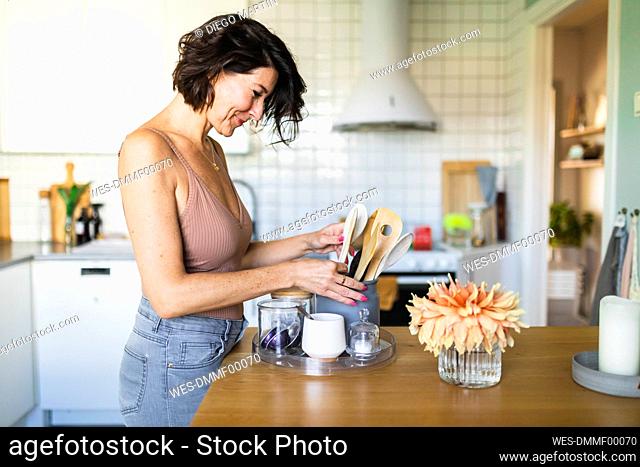 Smiling woman organizing spoons in container at kitchen counter