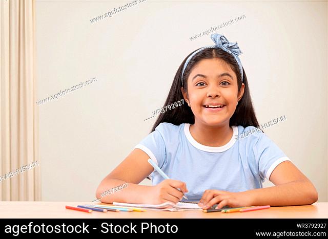 Portrait of cheerful girl writing on notebook against white background