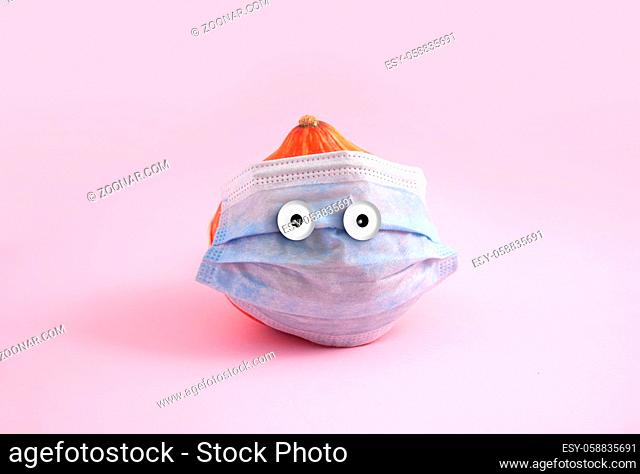 Pumpkin with medical face mask and funny eyes. Pink background, creative minimal concept. High quality photo