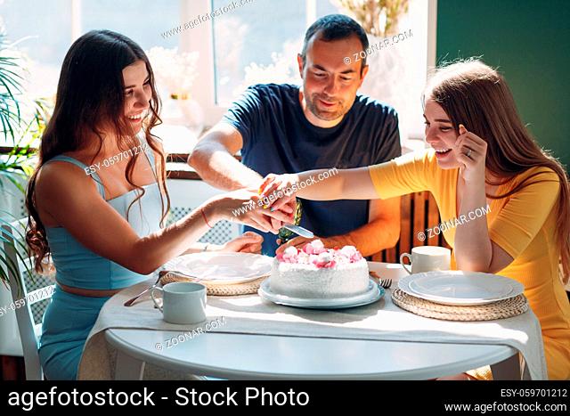 Man and young woman sit in home apartment kitchen with cake on table and celebrating birthday