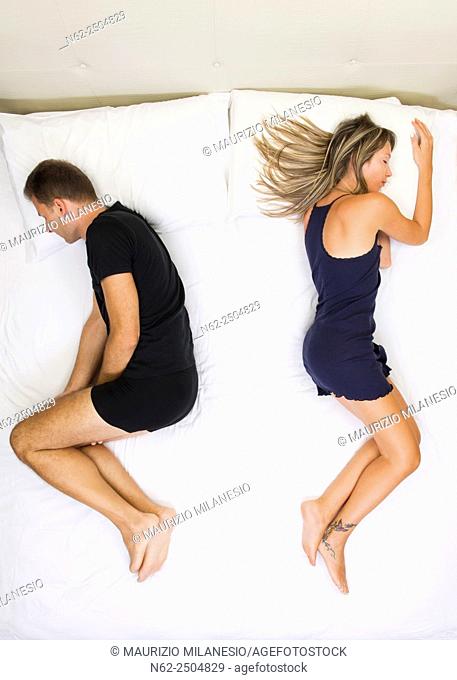 Unhappy couple sleeping far away from each other on bed top view