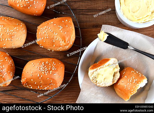 High angle view of sesame dinner rolls on a wire rack, with bread plate, and butter crock and knife