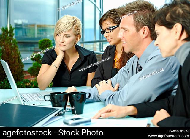 Group of young business people sitting in a row at table on office terrace outdoor, talking and working on laptop computer