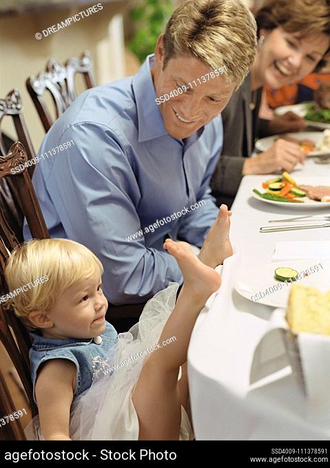 Father smiling at toddler with feet on dinner table