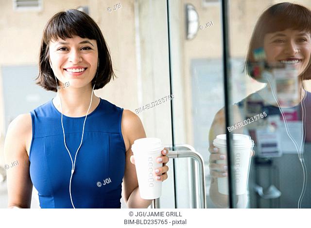 Hispanic woman drinking coffee and listening to earbuds