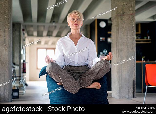 Blond businesswoman meditating while sitting on beanbag at home
