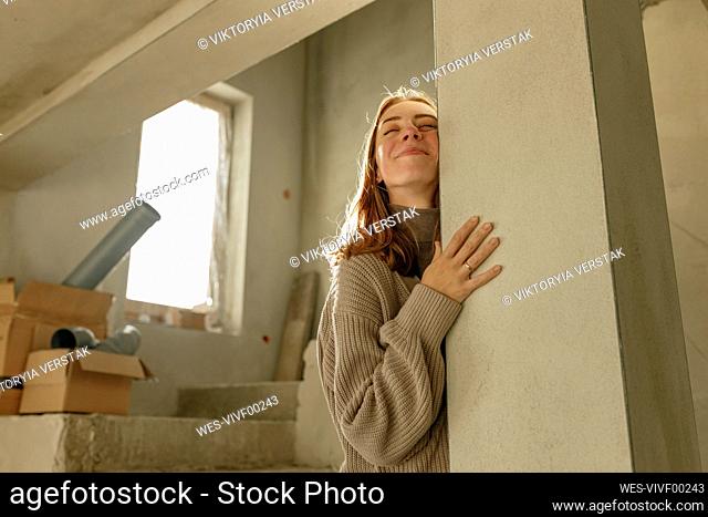 Smiling young woman hugging column at home