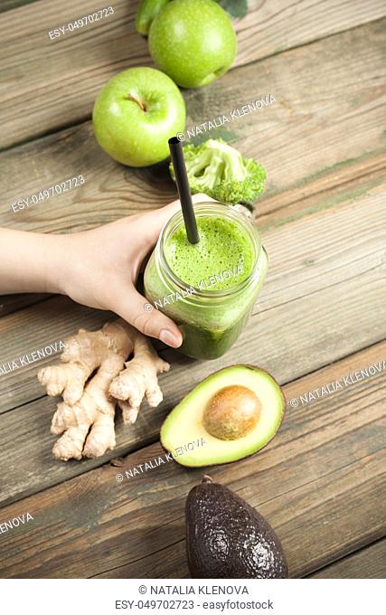 Mason jar mug filled with green smoothie In hand on wooden rustic table. Green healthy food, vegetarian, clean eating concept. Top view, copyspace