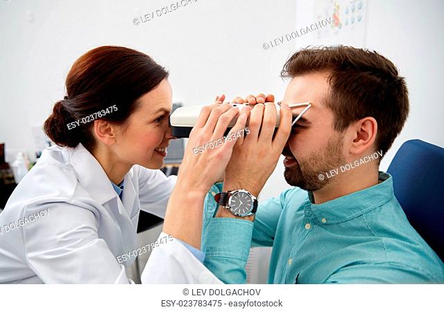 health care, medicine, people, eyesight and technology concept - optometrist with pupilometer checking patient intraocular pressure at eye clinic or optics...