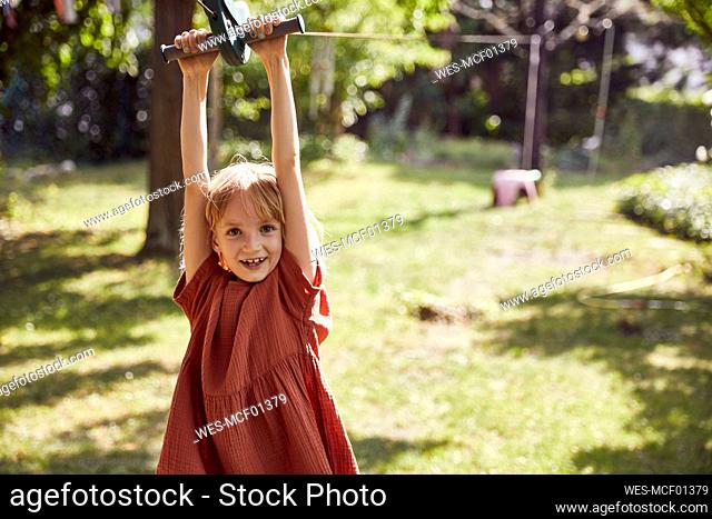 Cheerful girl hanging on outdoors play equipment in yard