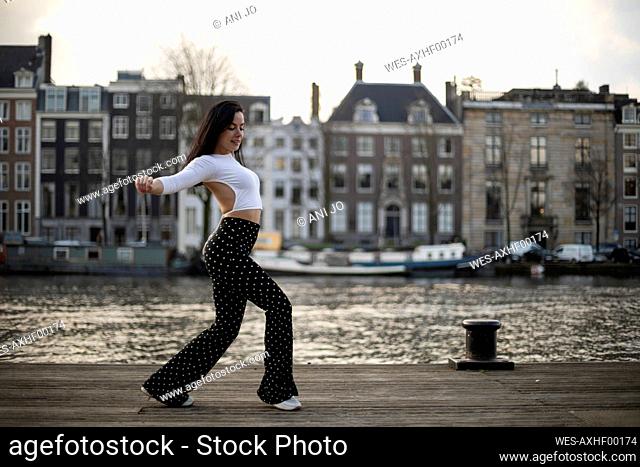 Woman dancing on pier near river against buildings