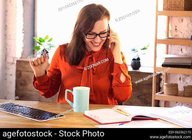 Businesswoman having phone call and grining. Cute smiling office lady discussing some work matters over phone while sitting at office table with some work...