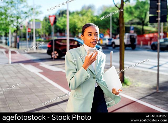 Young businesswoman sending voicemail through smart phone on footpath