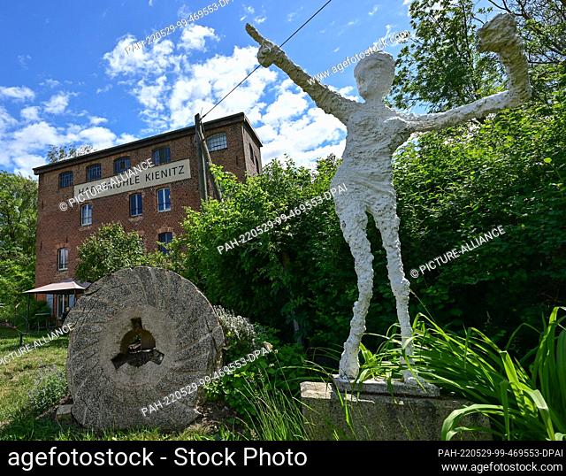 28 May 2022, Brandenburg, Kienitz: An old millstone and a sculpture stand in front of the building of cafe, gallery and vacation apartment of the harbor mill...
