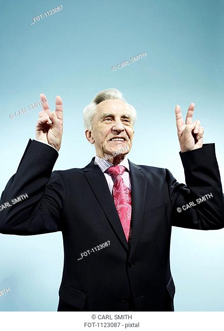 A senior man with both hands raised making peace signs
