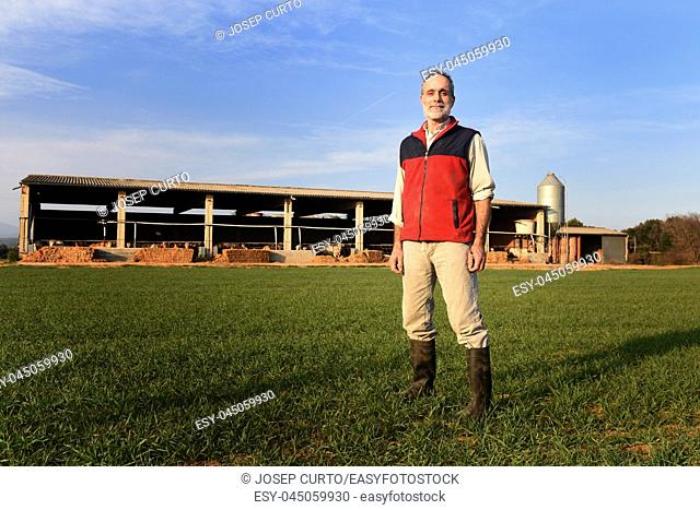 Portrait of a farmer in the countryside with a farm at sunset background