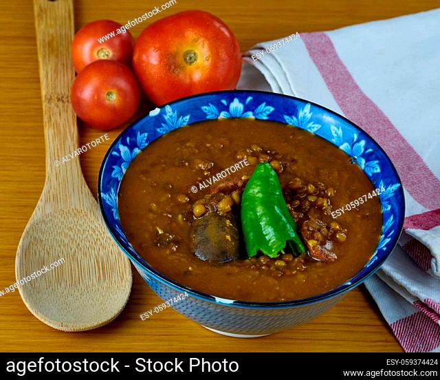 Homemade Lentil soup with Pork Sausages called Chorizo, Blood sausage called Morcilla and green pepper in a bowl decorated with tomatoes, a spoon and a napkin