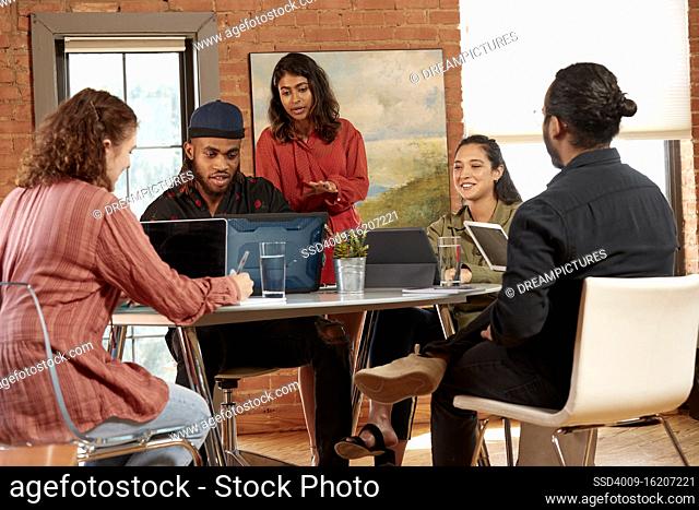 group of co-workers sitting at small table with their devices having discussion