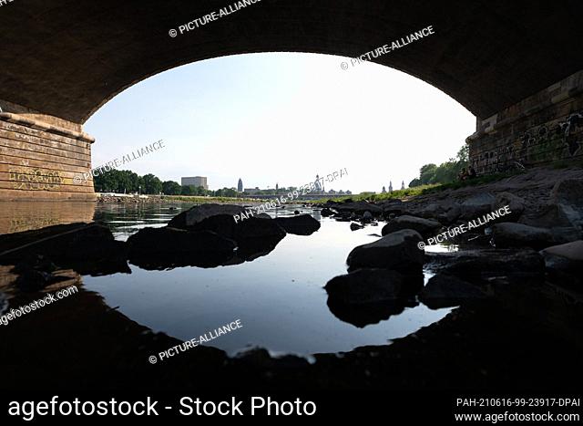 16 June 2021, Saxony, Dresden: Stones lie in the water on the banks of the Elbe against the backdrop of the Old Town, framed by the arch of the Albert Bridge