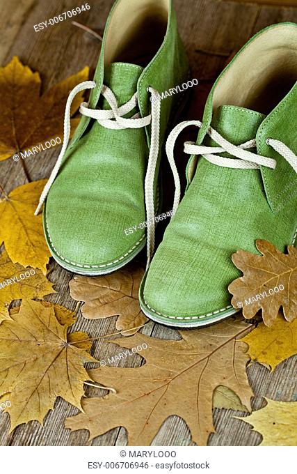 pair of green leather boots and yellow leaves on an old wooden floor