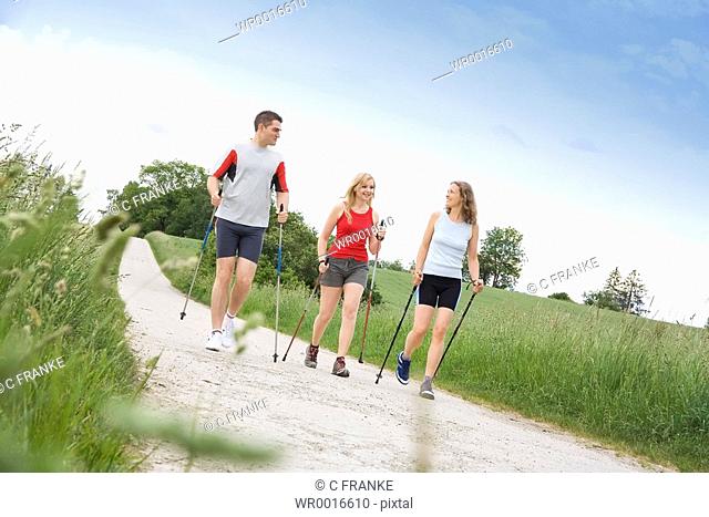 Two women and man walking with hiking poles on dirt road