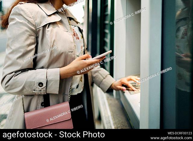 Woman using atm machine and mobile phone
