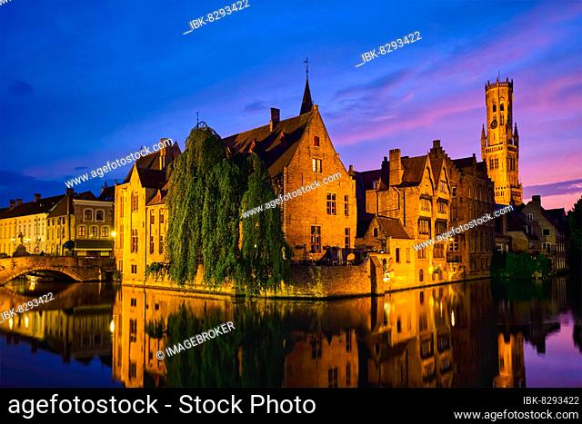 Famous view of Bruges tourist landmark attraction, Rozenhoedkaai canal with Belfry and old houses along canal with tree in the night